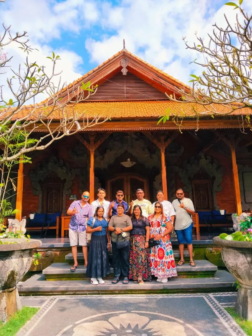 Tour group posing on the steps of a traditional wood-carved Balinese pavilion