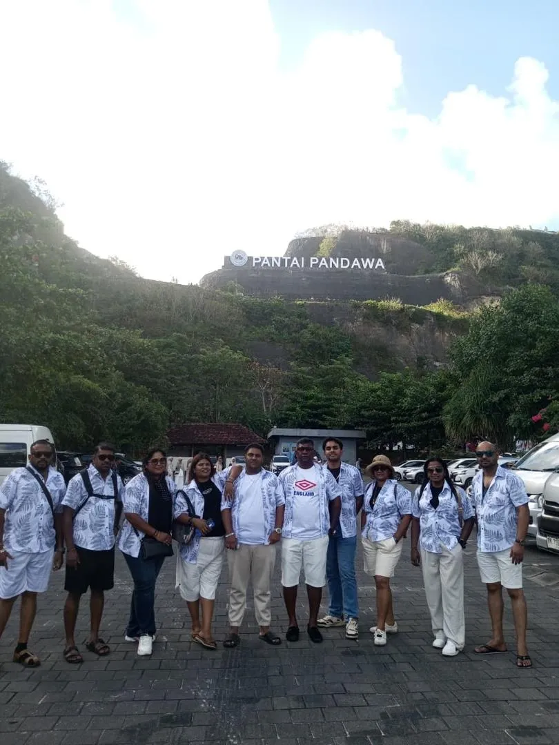 Tour group in matching batik shirts posing below the Pantai Pandawa beach signage in Bali