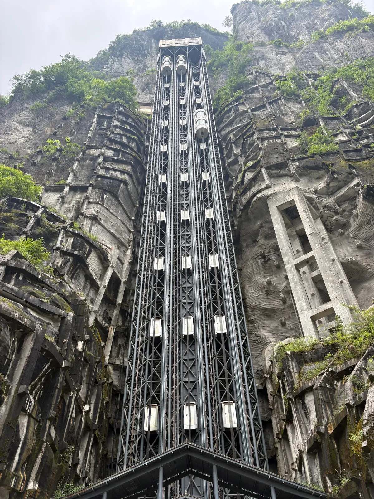 A tall glass-cabin elevator built into a sheer rock cliff face surrounded by greenery in China